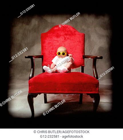 Three-month old boy sitting on red chair wearing neon yellow glasses