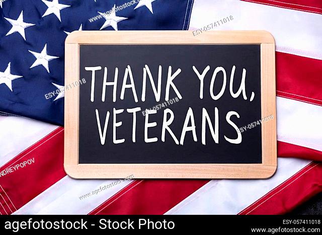 Top View Of Thank You Veterans Text Written On Slate Over American Flag