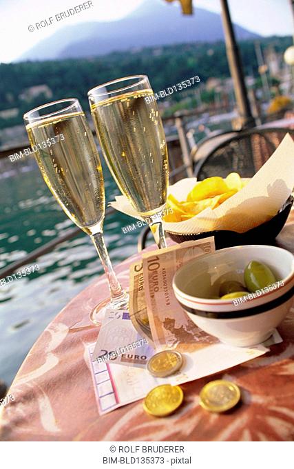 Glasses of champagne, chips, olive and money at sidewalk cafe