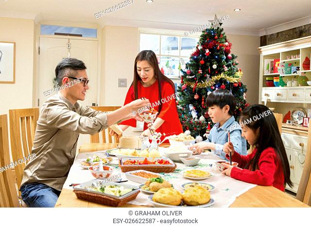 Chinese family enjoying their christmas dinner. They are eating traditional Chinese food. The parents are serving it round the table