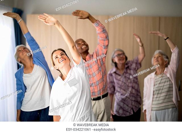 Smiling female doctor and seniors exercising with arms raised