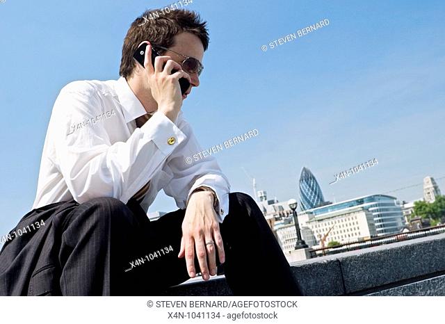 Young businessman uses mobile phone on south side of River Thames, London