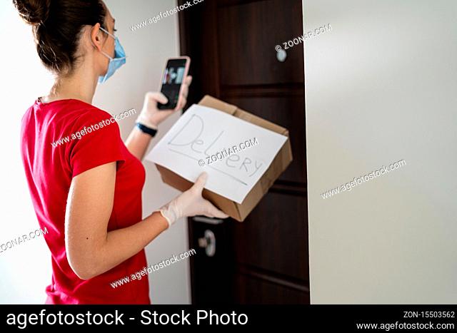 Young woman at home in gloves and mask taking delivery box from the floor. Contactless delivery concept. Covid-19 safety
