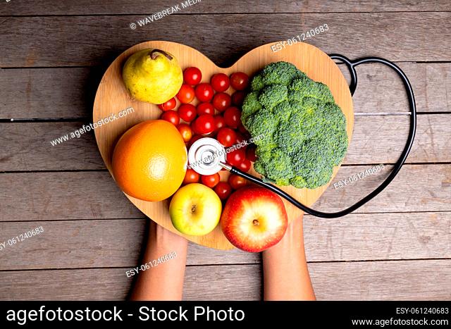 African american mid adult woman holding heart shape with vegetables, fruits, stethoscope on table