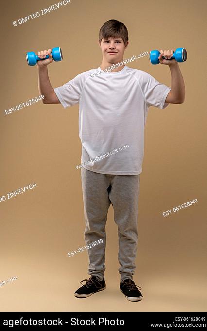 Full-size portrait of a teen holding a pair of dumbbells with arms bent and looking before him