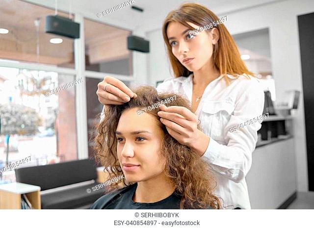 Doing new hairstyle in beaty salon with professional hairstyler. Young model having brown curly hair, pretty smile, dark eyes, looking forward