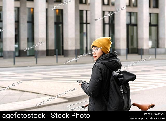 Woman with bicycle and smartphone in the city, Frankfurt, Germany