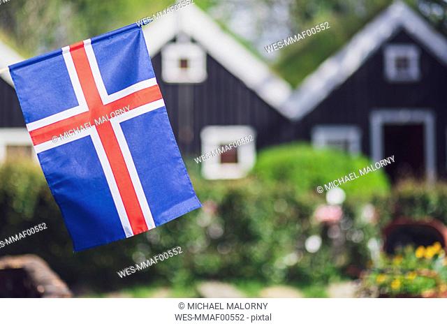 Iceland, Iceland national flag in the foreground, typical icelandic houses with grass on the roof in the background