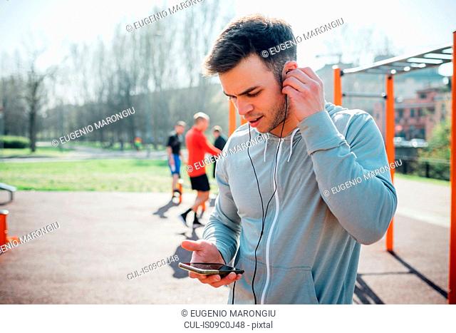 Calisthenics class at outdoor gym, young man putting in earphones
