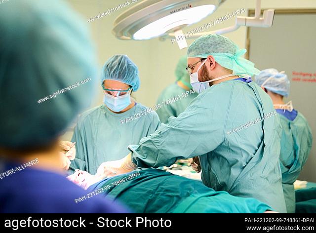 PRODUCTION - 30 November 2022, Berlin: Olexander Jazkowyna, Ukrainian surgeon, helps with an operation at Unfallkrankenhaus Berlin, while Virginia Galati