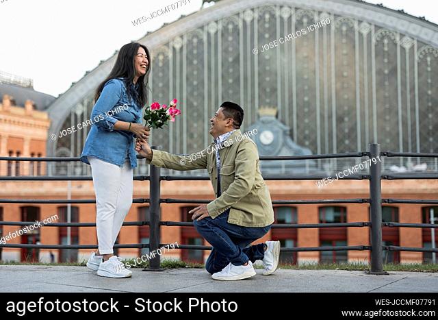 Happy man giving flowers to woman and proposing at footpath on Valentine's day