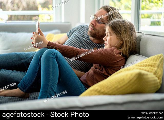 daughter taking selfie through phone with father on sofa