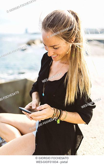 Smiling young woman at the seafront using cell phone