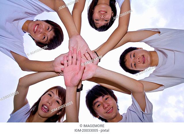 Five teenagers reaching hands out in a stack and looking at the camera, Teenager