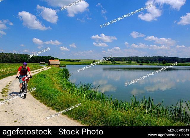 Germany, Franconia, Uehlfeld, Mature man cycling along carp pond