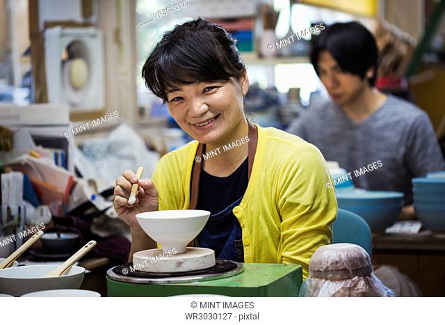 Smiling woman and man sitting in a workshop, working on Japanese porcelain bowls