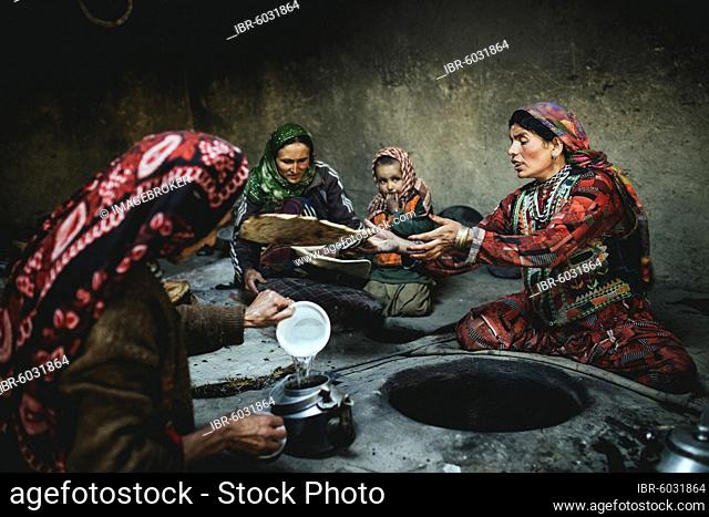 Three woman and a child baking flat bread, smoking kitchen in a mud house with stone oven, sedentary Wakhi, Khandud, Wakhan corridor, Afghanistan, Asia