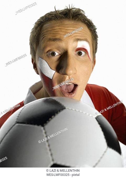 Young man with Poland flag painted on face holding soccer ball, mouth open, close-up