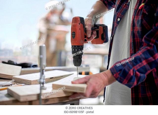 Cropped shot of female carpenter drilling wood in furniture making workshop