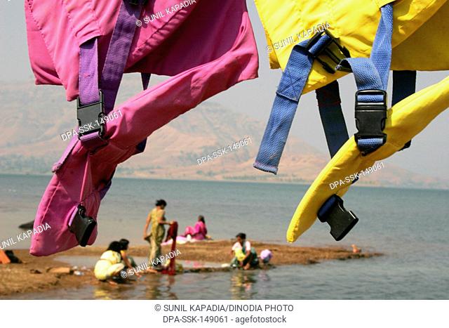 Abstract of colourful lifeguards hanging for drying maharashtrian ladies washes cloths at bank of lake at Dhom Dam ; Wai ; Maharashtra ; India
