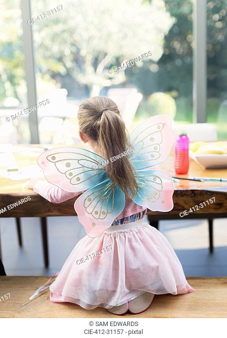 Girl in fairy wings coloring at dining table