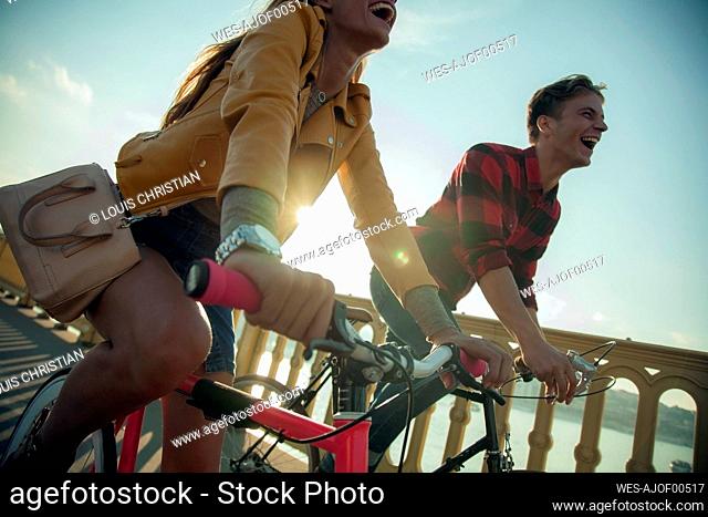 Happy couple riding bicycle against sky during sunny day