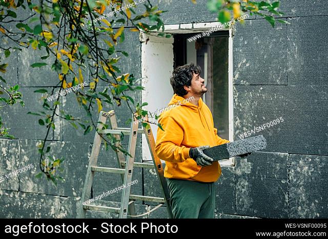 Man holding polystyrene looking at wall of house
