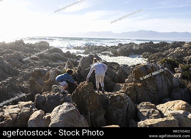 Two children exploring the jagged rocks and rock pools on the Atlantic Ocean coastline, De Kelders, Western Cape, South Africa