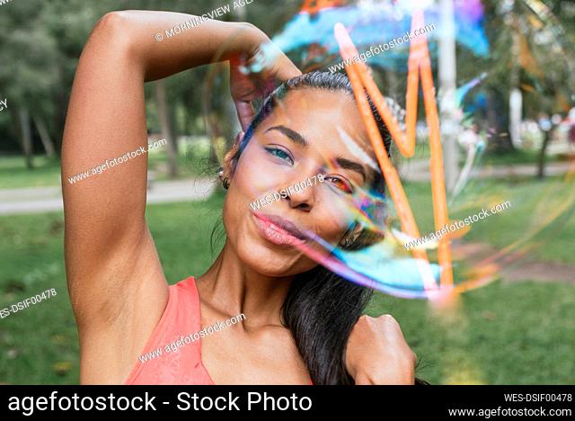 Sportswoman doing stretching exercise seen through soap bubble at park