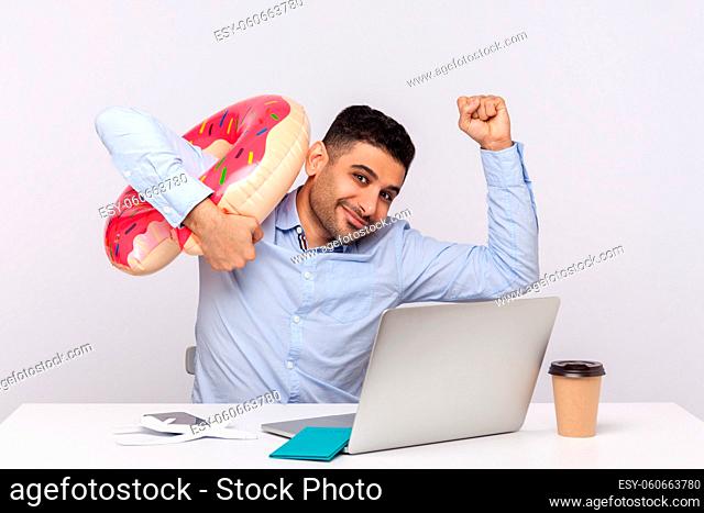 Happy man employee raising hands about to run away with rubber ring from his office workplace, hurry to rest on weekend trip, travel and holiday tour