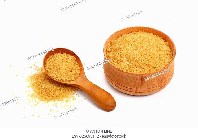 Wooden scoop spoon and bowl full of brown cane sugar with pinch of sugar spilled around isolated on white background