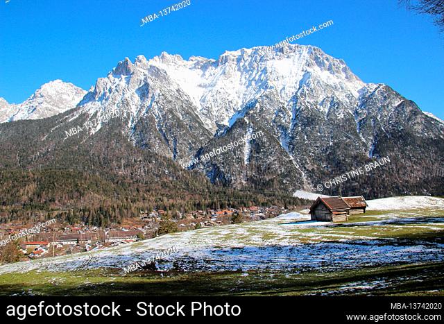 Spring walk near Mittenwald, the Karwendel Mountains all in white, in the foreground the slightly snowed-in spring meadow with hay barn, overview of the area