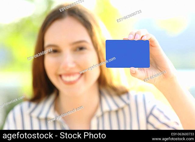 Happy woman showing blank credit card at camera in nature