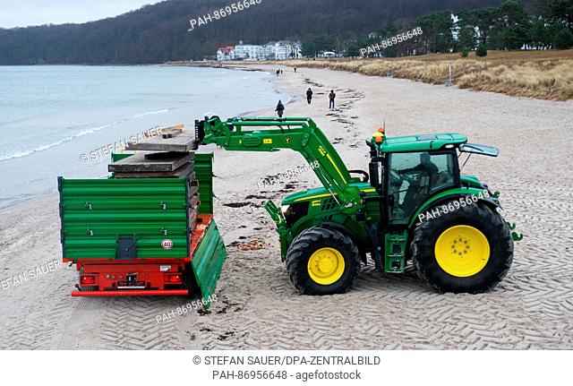 The owner of a waterfront cafe and snack store uses a tractor to load the parts of a wooden boardwalk onto a trailer on the island of Ruegen in northeastern...