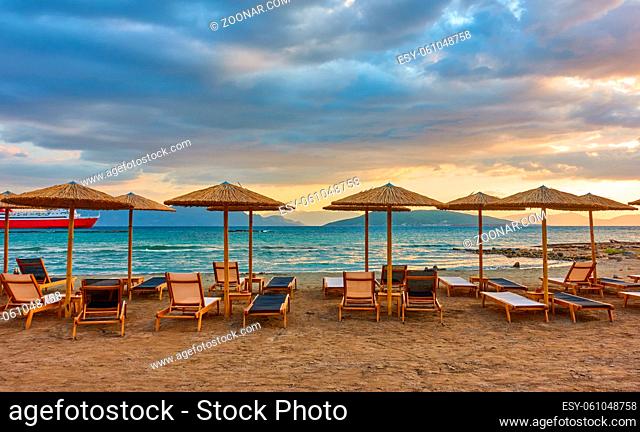 Panorana of empty beach with deck chairs and straw umbrellas by the sea and colorful clouds at sunset, Aegina Island, Greece - Greek landscape - seascape