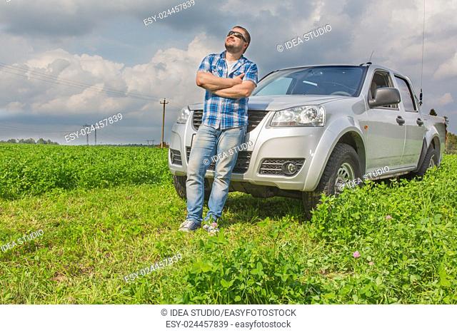 Man standing in front of car leaned on cowl and looking up in the sky