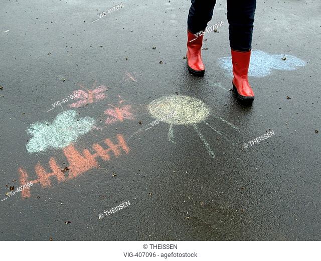 MR legs of a person woman with red rubberboots going for a walk in rainy weather on a wet road with black asphalt surface with a drawing of children kids with...