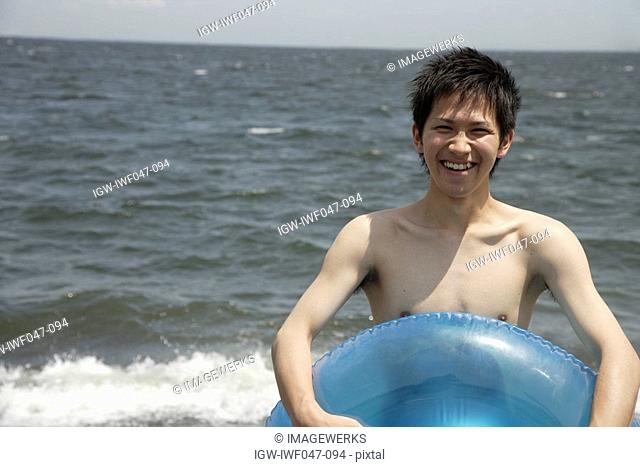 Portrait of a young man holding lifebuoy on beach