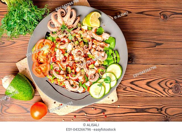 top view of salad with tentacles of octopus, lime, avocado and lettuce, decorated lime, cucumber, tomato, sprigs of pea leaves and dry peppers, natural seafood