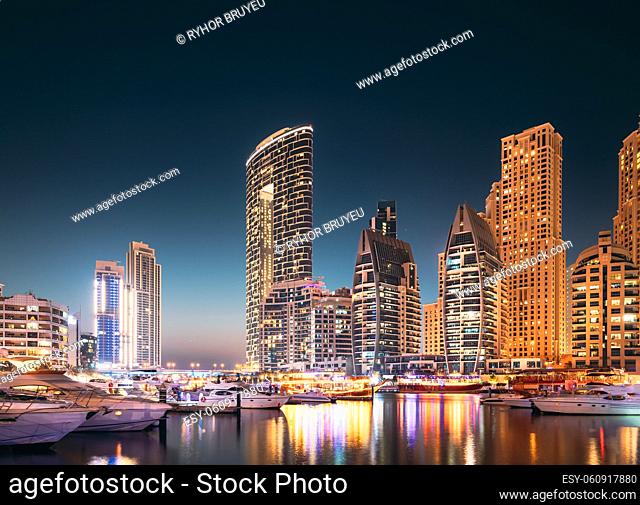 Dubai Marina Port, UAE, United Arab Emirates. Jetty With Many Moored Yachts, Sightseeing Boat In Evening Night Illuminations