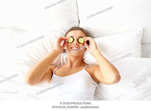 beautiful woman applying cucumbers to face at home