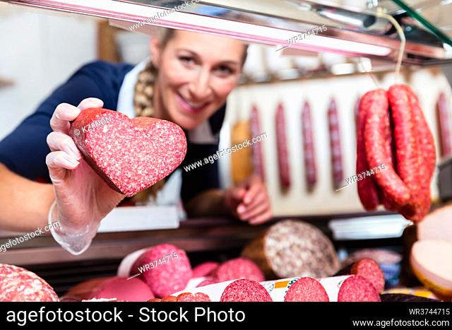 Sales woman in meat shop showing a heart shaped sausage to customer