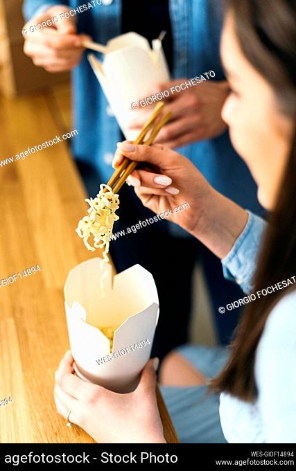 Woman eating noodles with chopsticks in kitchen