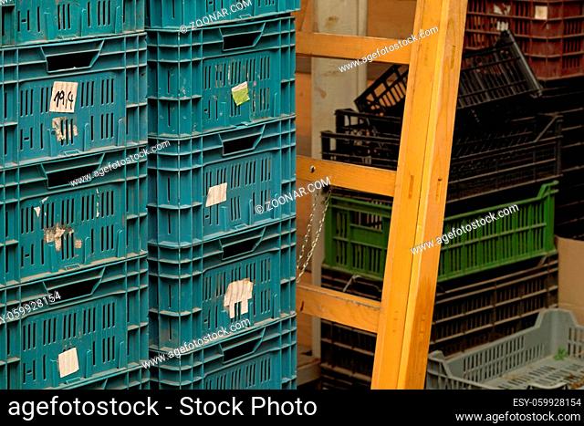 Plastic boxes stacked in warehouse room, wooden ladder and more containers at background