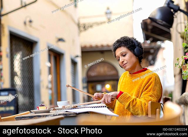 Italy, Tuscany, Pistoia, Woman practicing with drumsticks in outdoor cafe
