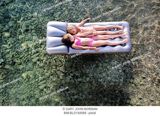 Caucasian girls floating on raft in lake