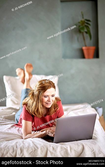 Smiling woman using laptop lying on bed at home