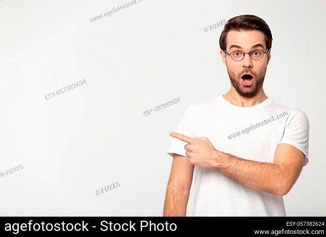 Amazed man in glasses point finger aside at copy space pose isolated on grey background, bespectacled guy excited by unbelievable offer of eyewear optics store