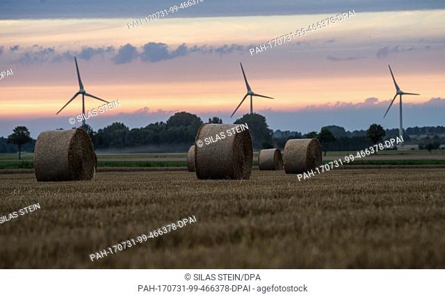 Hay bales in a field in front of a wind farm at sunset in Wennigsen, Germany, 31 July 2017. Photo: Silas Stein/dpa. - Wennigsen/Lower Saxony/Germany