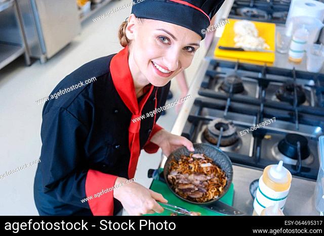 A female using tongs to grab noodles out of a frying pan